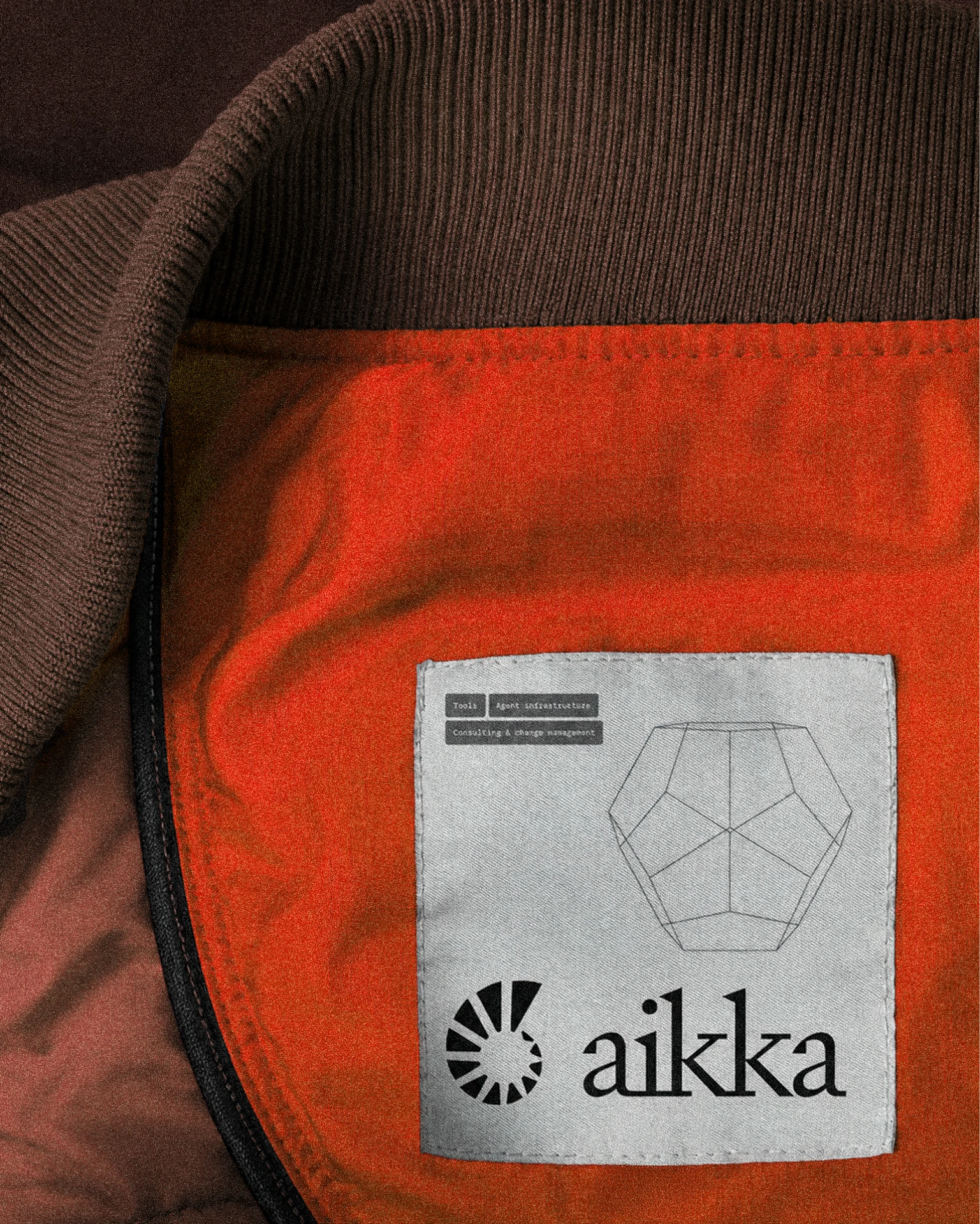 Aikka woven label with the logo and a wireframe shell, sewn inside an orange jacket