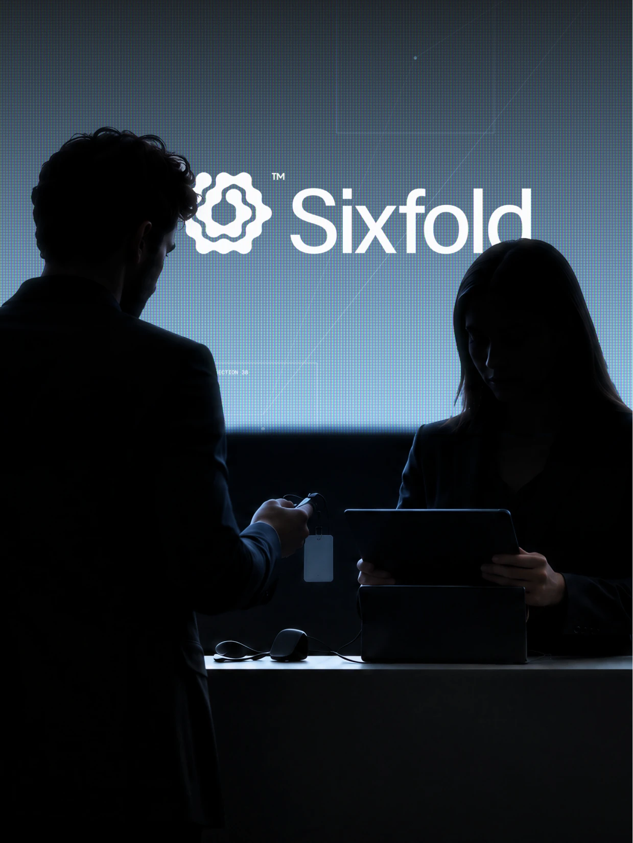 Two people at a counter in front of a large Sixfold logo on a pale blue wall