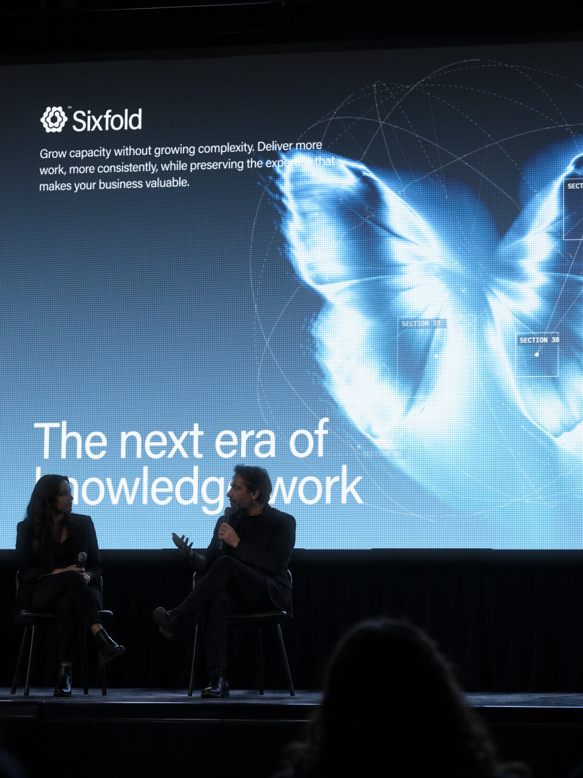 Two speakers on stage under a Sixfold screen reading The next era of knowledge work
