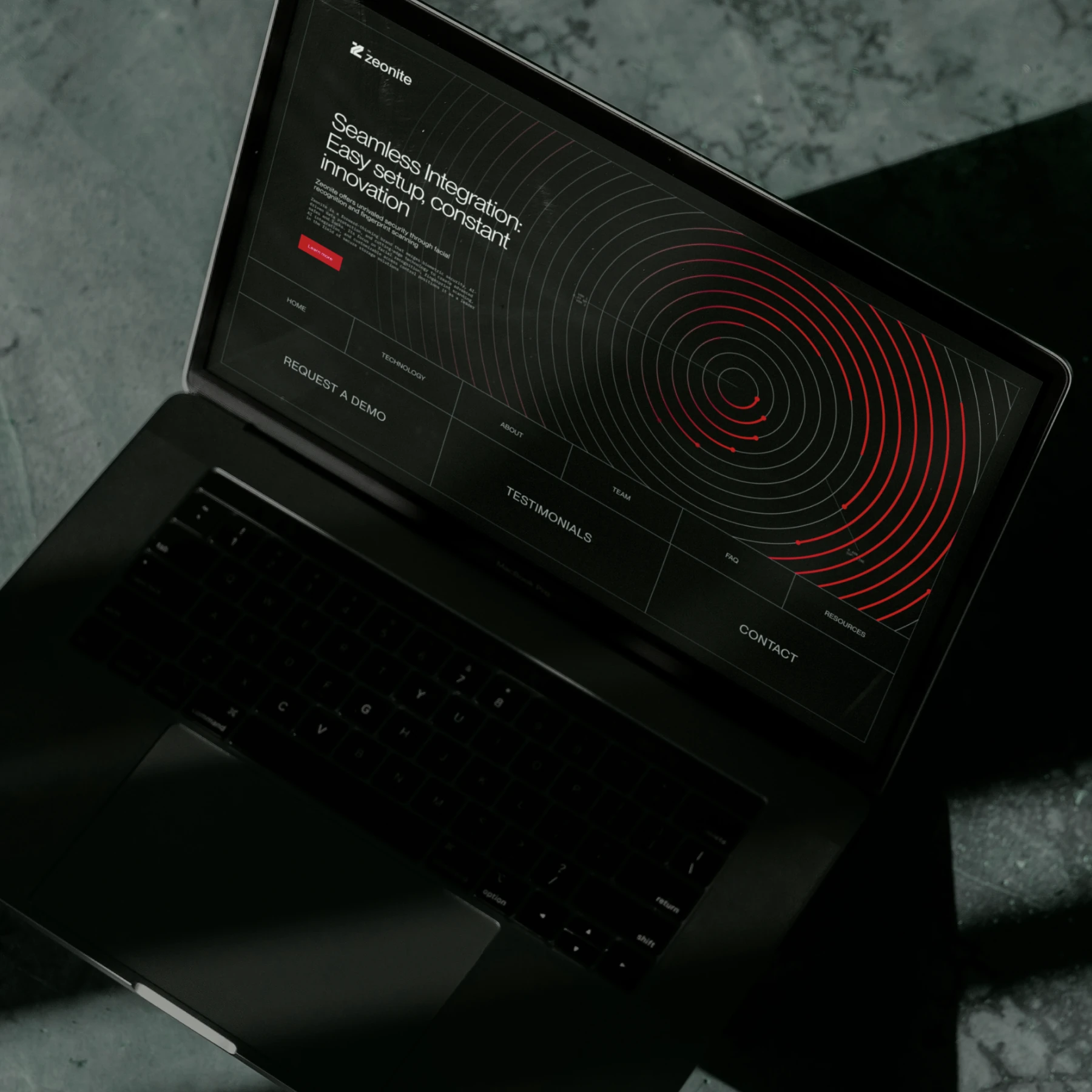 Laptop on stone showing the Zeonite website with red fingerprint rings